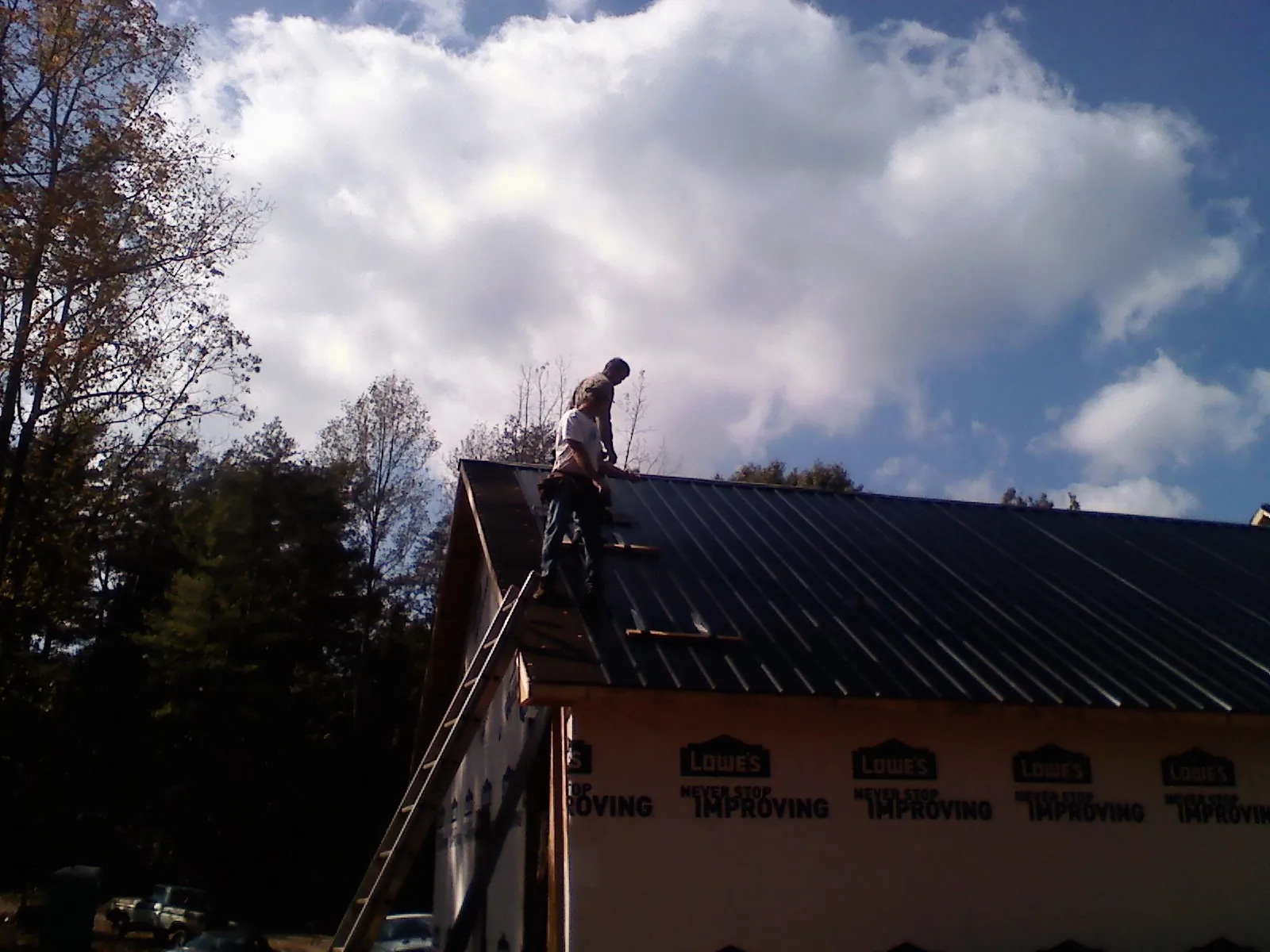 Roofer fastening dark metal panels high against a cloudy sky, from a Roof Inspection job in Wolcott