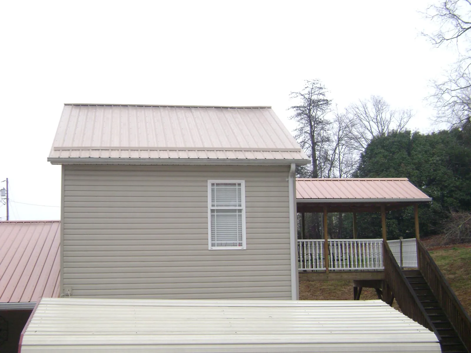 Tan metal roofs on a two story addition and attached porch, from a Roof Replacement job in Wolcott