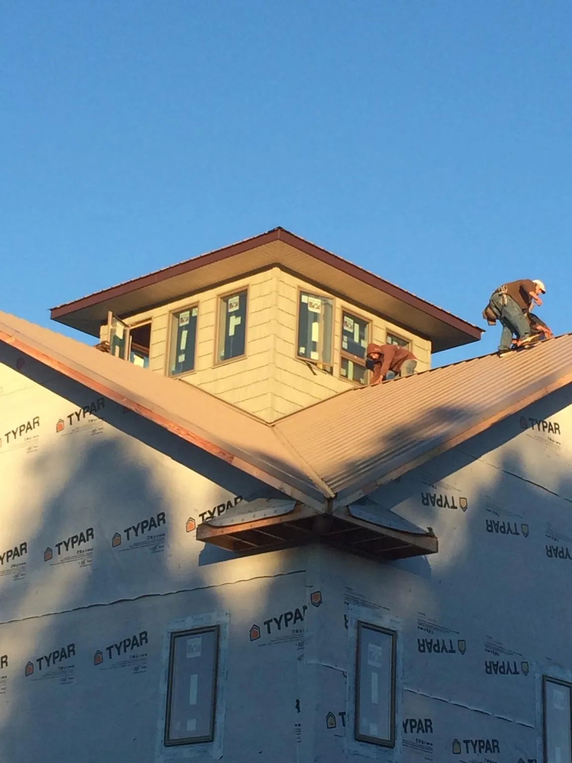 Roofers working around a rooftop cupola on a new metal roof at sunset — Roof Waterproofing in Wolcott by Roofing Brothers